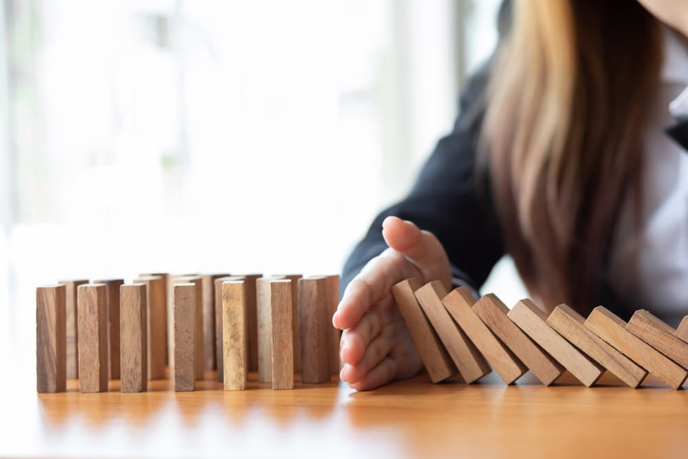 Businesswoman prevents wooden block fall, risk management concept.